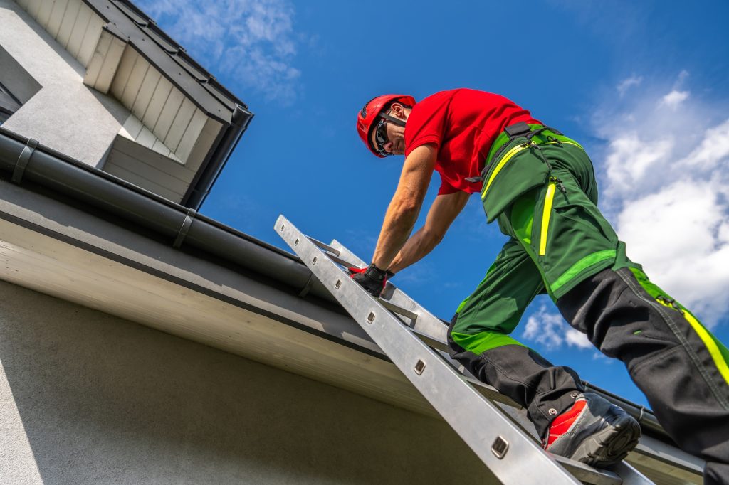 Professional Maintenance Worker Climbing a Ladder to Repair Roof Gutter on a Sunny Day