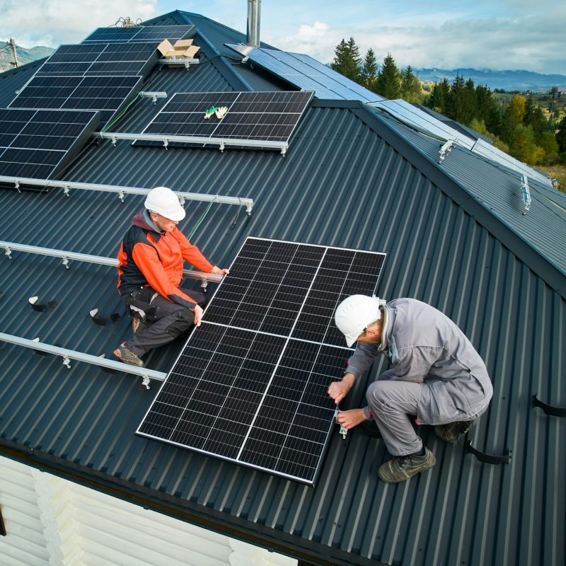 Technicians installing photovoltaic solar panels on roof of house.